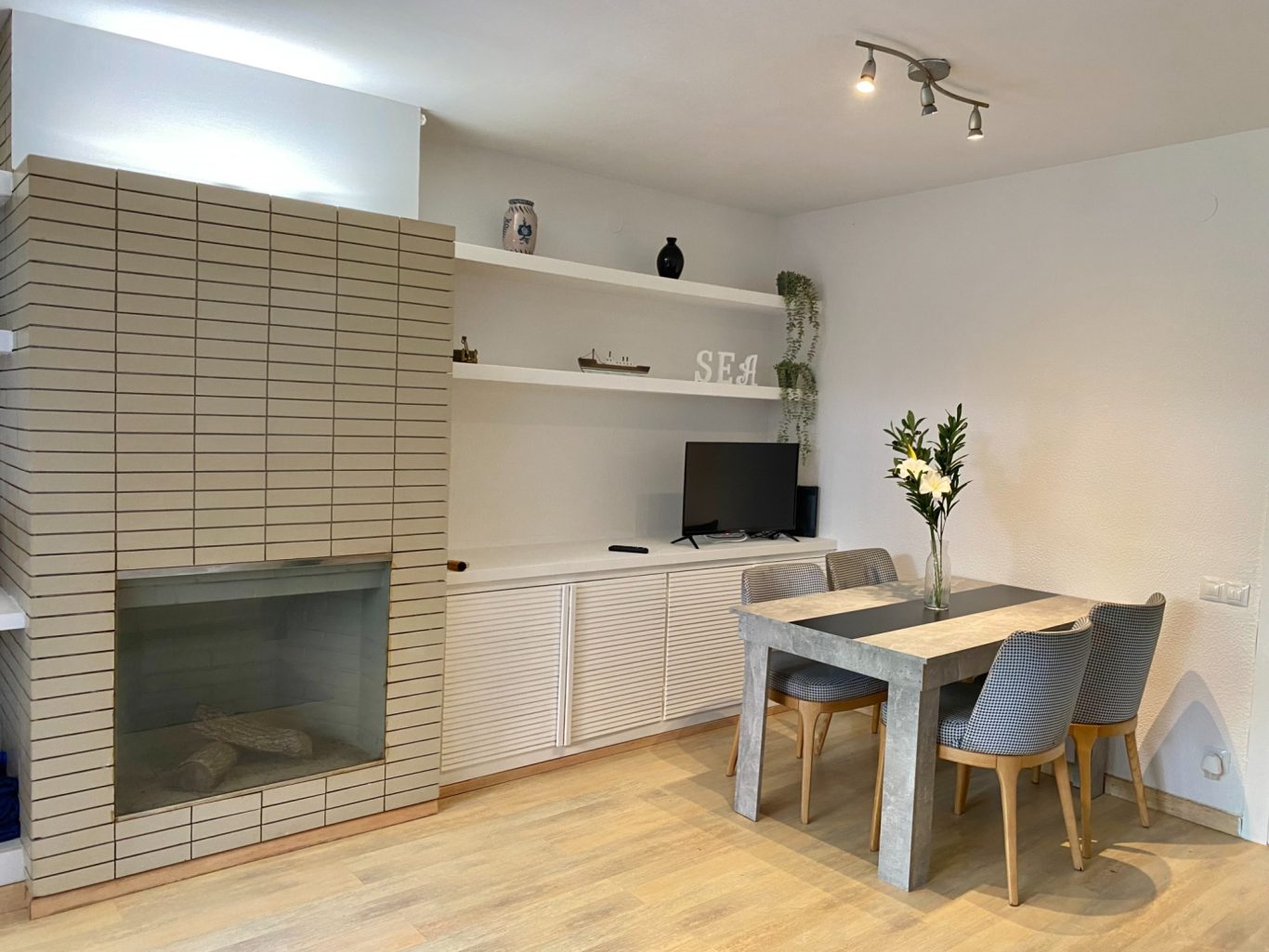 Salón moderno con estanterías, comedor y chimenea. Muebles en tonos claros y decoración minimalista.