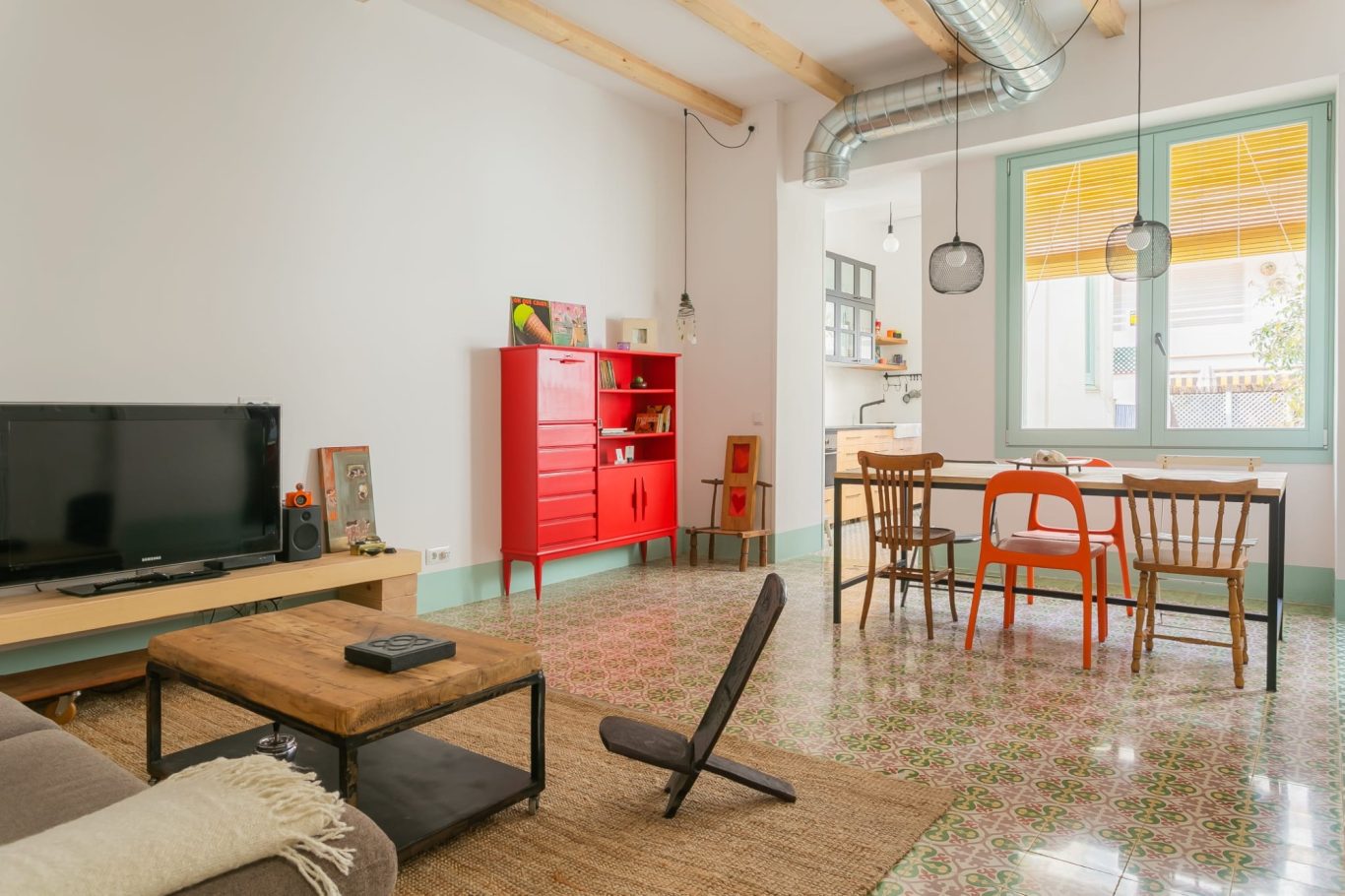 Salón moderno con sofá, mesa de comedor, mueble rojo y suelo de baldosas coloridas.